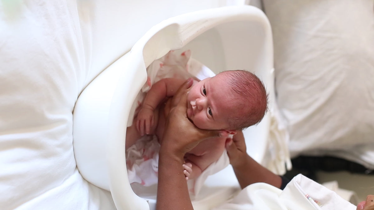 Parent holding a newborn in the water during the first bath