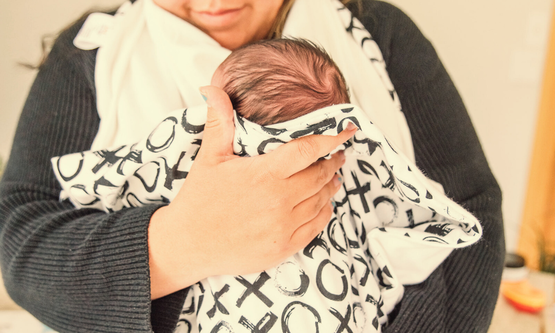 Person holding a baby wrapped in a patterned carrier indoors.
