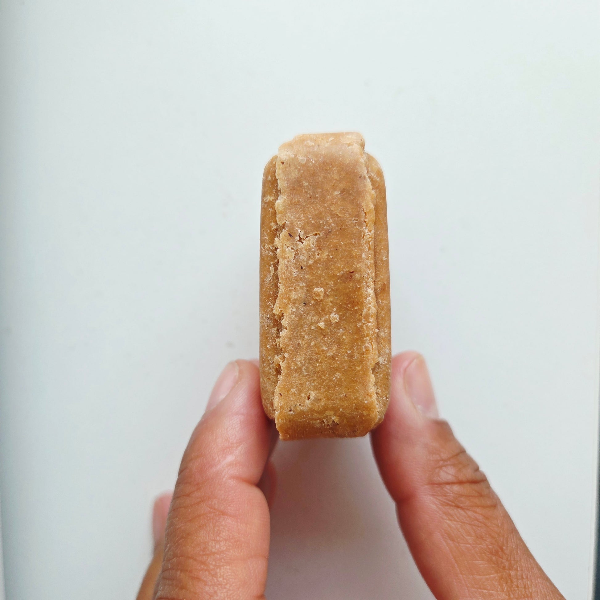 A hand holding a small, rectangular, tan-colored solid bar against a plain white background.
