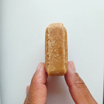 A hand holding a small, rectangular, tan-colored solid bar against a plain white background.