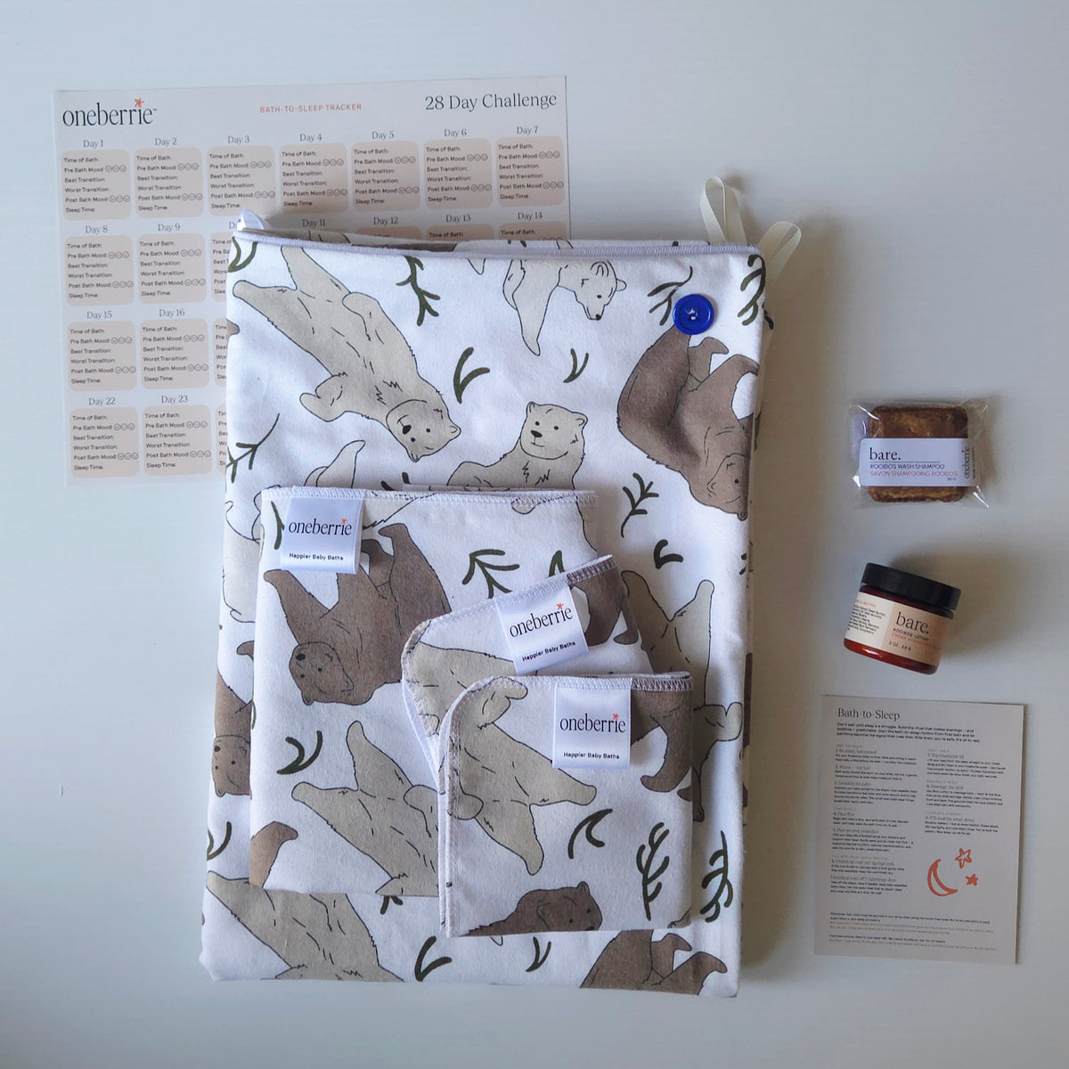 A Bath to Bed Complete set by OneBerrie, featuring  Three bears pattern with a grizzly, brown bear and polar bear, a matching bath swaddle, a washcloth, a 2oz Bare. lotion, 30g Bare. shampoo wash, a 28-day challenge tracker sheet, and an instruction card on a light gray background.