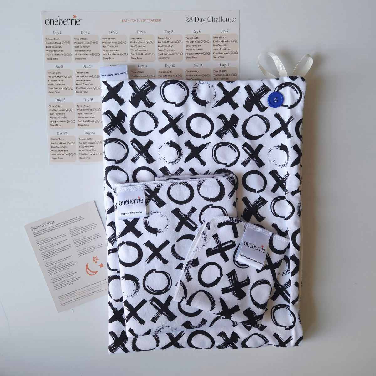 A Bath to Bed Core set by OneBerrie, featuring  Love you More XO black pattern on white background,, a matching bath swaddle, a washcloth, a 28-day challenge tracker sheet, and an instruction card on a light gray background