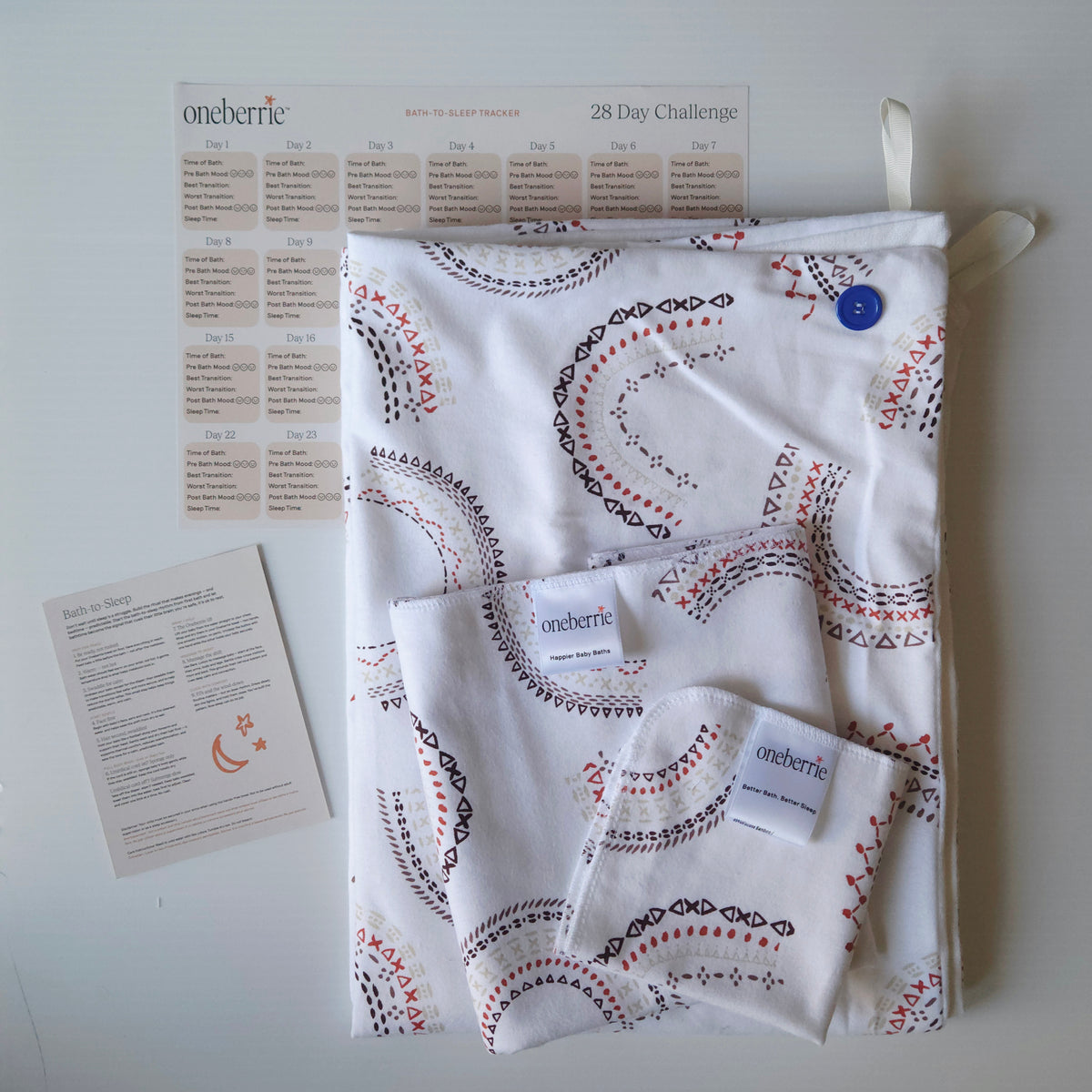 A Bath to bed core set by OneBerrie, featuring a geometric pattern in arches like a rainbow, a matching bath swaddle, a washcloth, a 28-day challenge tracker sheet, and an instruction card on a light gray background