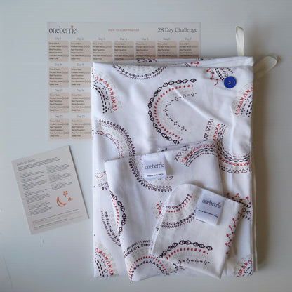 A Bath to bed core set by OneBerrie, featuring a geometric pattern in arches like a rainbow, a matching bath swaddle, a washcloth, a 28-day challenge tracker sheet, and an instruction card on a light gray background