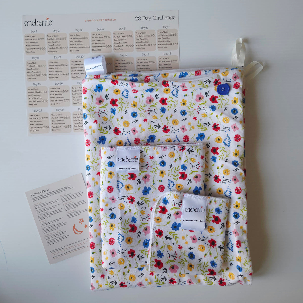 A Bath to Bed set by OneBerrie, featuring  Wild flower colourful pattern on white background, a matching bath swaddle, a washcloth, a 28-day challenge tracker sheet, and an instruction card on a light gray background
