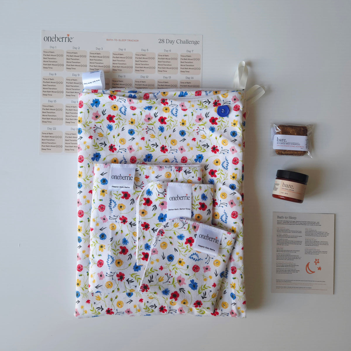 A Bath to Bed Complete set by OneBerrie, featuring the wild pattern with small colourful wildflowers, a matching bath swaddle, a washcloth, a wipe, a 2oz Bare. lotion and 30g Bare. Shampoo Wash bar, a 28-day challenge tracker sheet, and an instruction card on a light gray background.