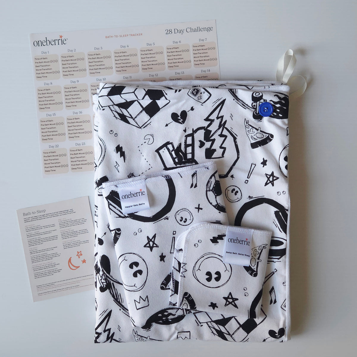 A Bath to Bed Core set by OneBerrie, featuring  Cool Dudes pattern with retro designs in black ink on a white background, a matching bath swaddle, a washcloth, a 28-day challenge tracker sheet, and an instruction card on a light gray background.