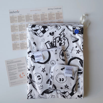 A Bath to Bed Core set by OneBerrie, featuring  Cool Dudes pattern with retro designs in black ink on a white background, a matching bath swaddle, a washcloth, a 28-day challenge tracker sheet, and an instruction card on a light gray background.