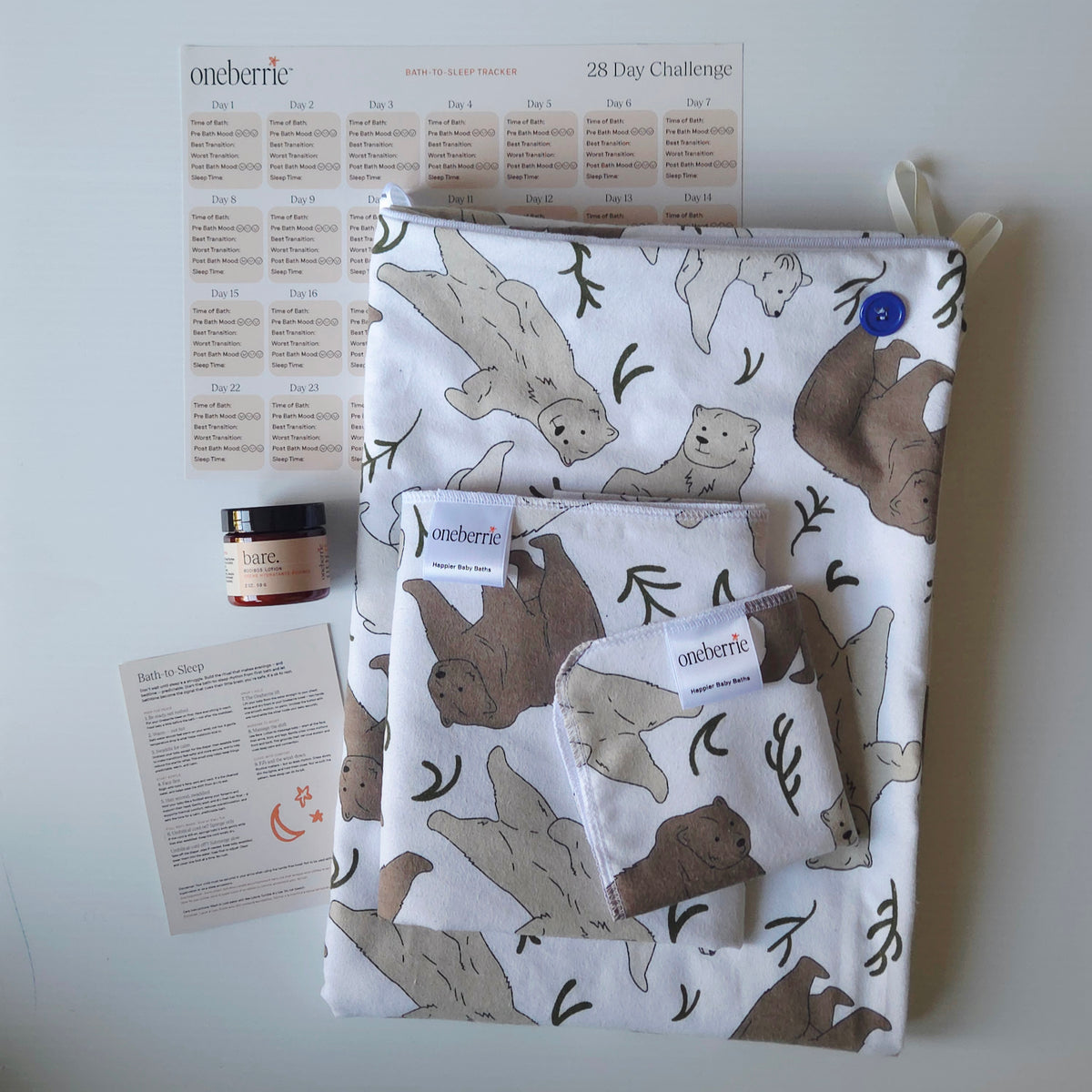 A Bath Bundle set by OneBerrie, featuring  Three bears pattern with a grizzly, brown bear and polar bear, a matching bath swaddle, a washcloth, a 2oz Bare. lotion, a 28-day challenge tracker sheet, and an instruction card on a light gray background.