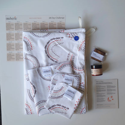 A Bath to bed complete set by OneBerrie, featuring a geometric pattern in arches like a rainbow, a matching bath swaddle, a washcloth, a 2oz Bare. Lotion, 30g Bare. Shampoo Wash, a 28-day challenge tracker sheet, and an instruction card on a light gray background