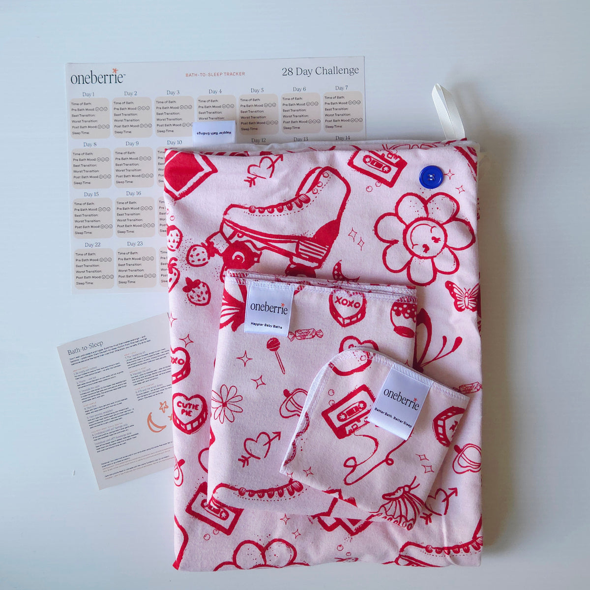 A Bath to bed core set by OneBerrie, featuring  pink ladies retro pattern with red designs on a pink background, a matching bath swaddle, a washcloth, a 28-day challenge tracker sheet, and an instruction card on a light gray background