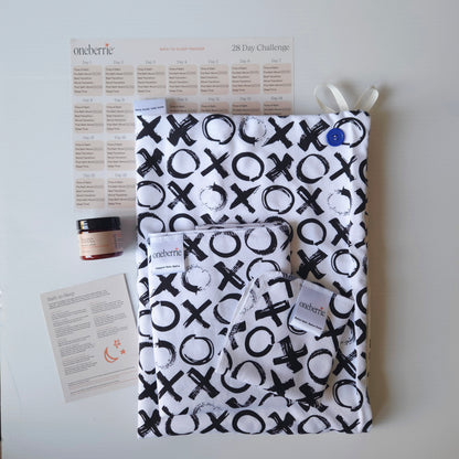 A Bath Bundle set by OneBerrie, featuring  Love you More XO black pattern on white background,, a matching bath swaddle, a washcloth, a 2oz Bare. Lotion, a 28-day challenge tracker sheet, and an instruction card on a light gray background