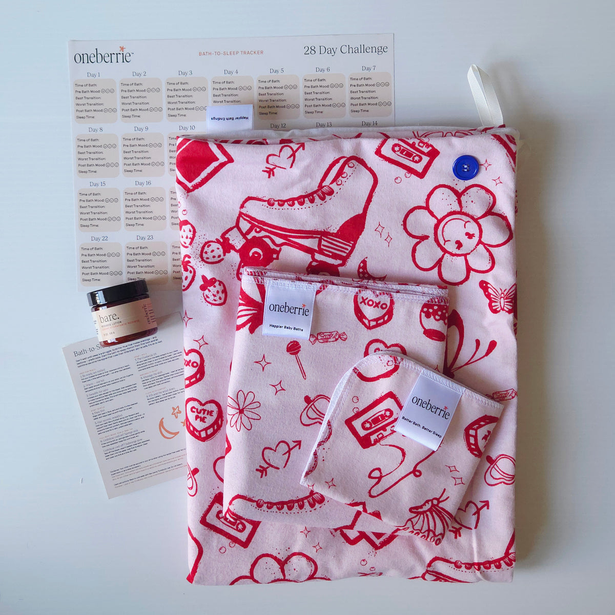 A Bath Bundle set by OneBerrie, featuring  pink ladies retro pattern with red designs on a pink background, a matching bath swaddle, a washcloth, a 2oz Bare. Lotion, a 28-day challenge tracker sheet, and an instruction card on a light gray background