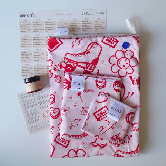 A Bath Bundle set by OneBerrie, featuring  pink ladies retro pattern with red designs on a pink background, a matching bath swaddle, a washcloth, a 2oz Bare. Lotion, a 28-day challenge tracker sheet, and an instruction card on a light gray background