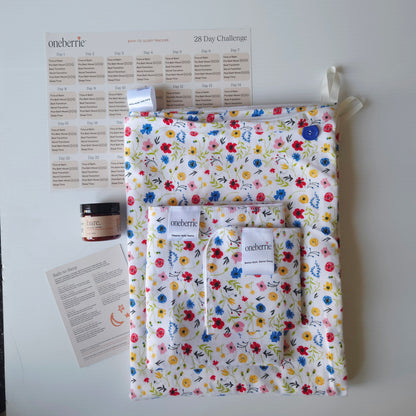 A Bath Bundle set by OneBerrie, featuring  wildflower colourful pattern on white background, a matching bath swaddle, a washcloth, a 2oz Bare. Lotion, a 28-day challenge tracker sheet, and an instruction card on a light gray background