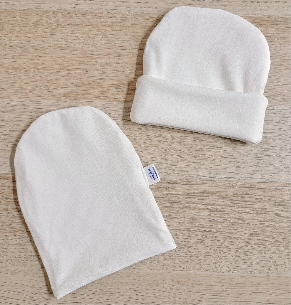 Two baby hats on a table. One is folded and one is unfolded.