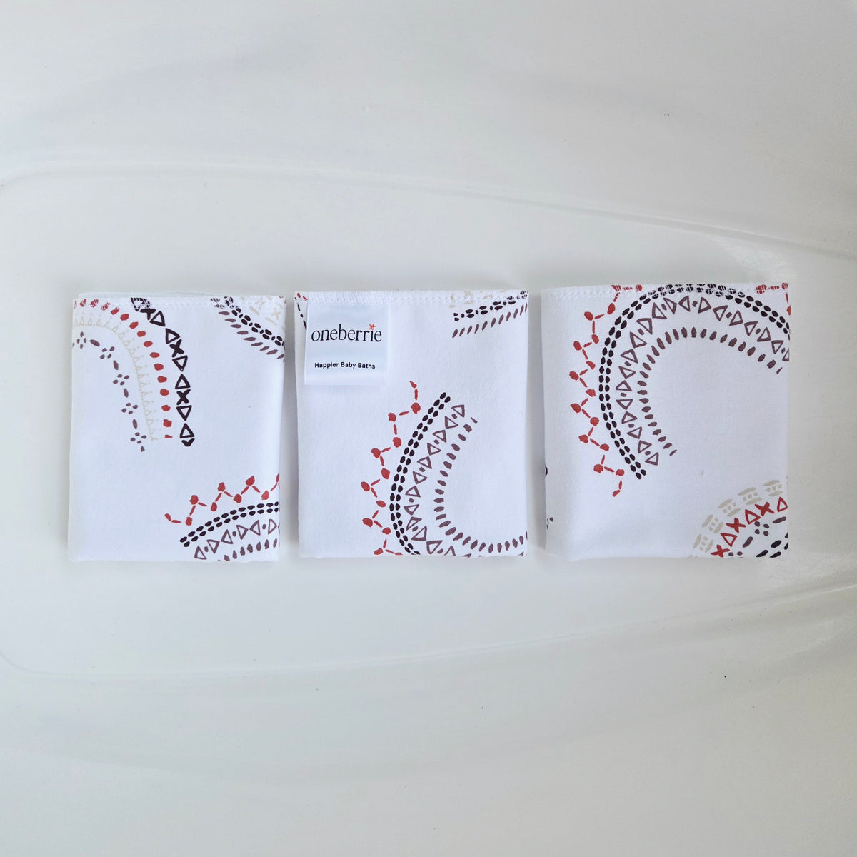 Three folded washcloths arranged side by side on a white background. Each washcloth has a decorative black and red embroidered-style geometric pattern, and the center pouch shows the brand name 'Oneberrie' printed on it