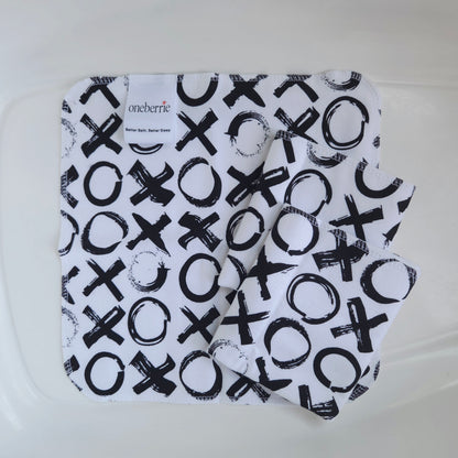 Three white flannel baby washcloths with a black graphic print of x's and o's, folded inside a clear plastic tub. The brand label 'oneberrie' is visible on the top left.