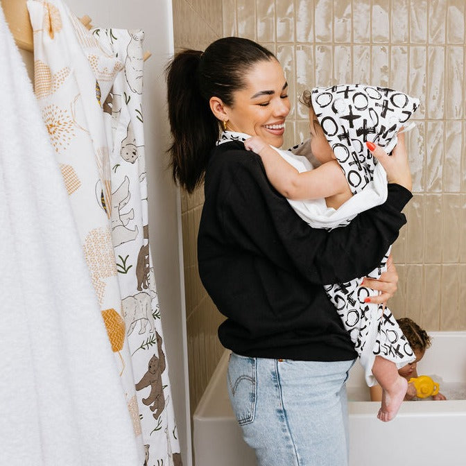 Mom wearing the Oneberrie towel lifts her baby out of the tub, already wrapped and hooded, while siblings play in the bath