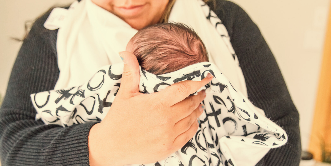 Person holding a baby wrapped in a patterned hands free towel after bath