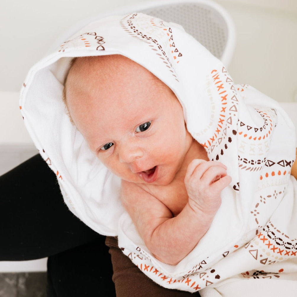 Newborn baby in a hooded Here comes the sun towel on moms lap after the bath. Baby is yawning.