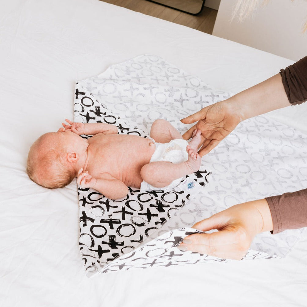 Newborn being swaddled in a XO cotton flannel swaddle with moms hands folding the ends