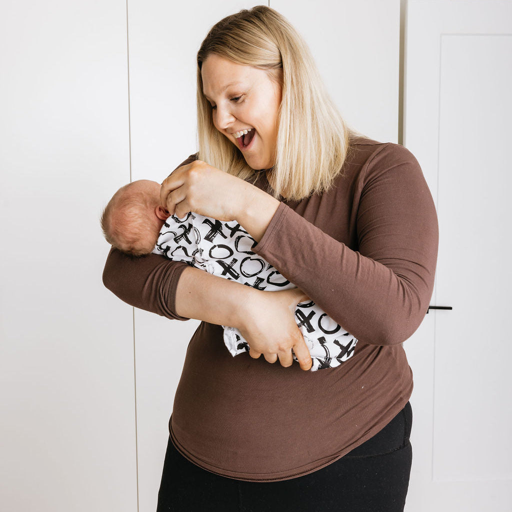 Woman holding a baby wrapped in a patterned blanket indoors.