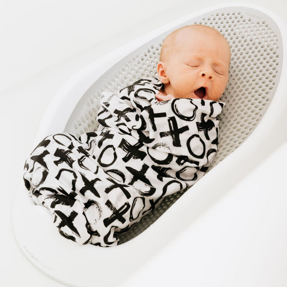 Newborn yawning, swaddled in the XO Oneberrie swaddle in a mesh bath seat
