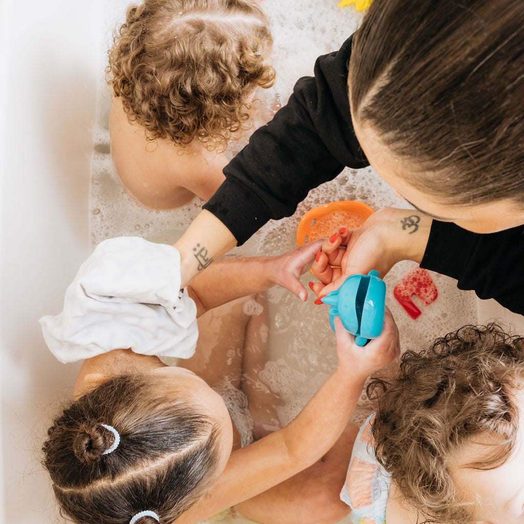 Three children in a bathtub with a woman, playing with toys and bubbles.