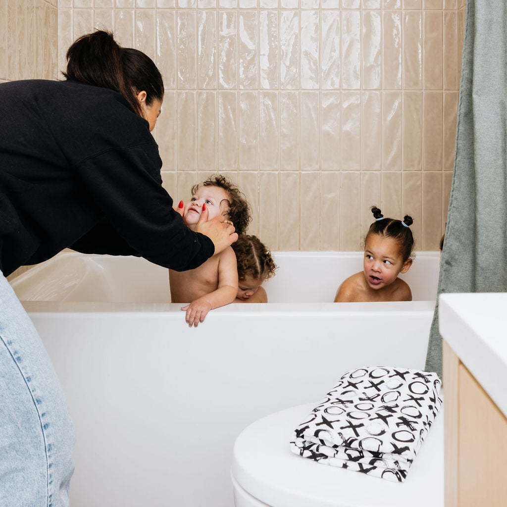 Woman and two children in a bathtub with a towel on the edge.