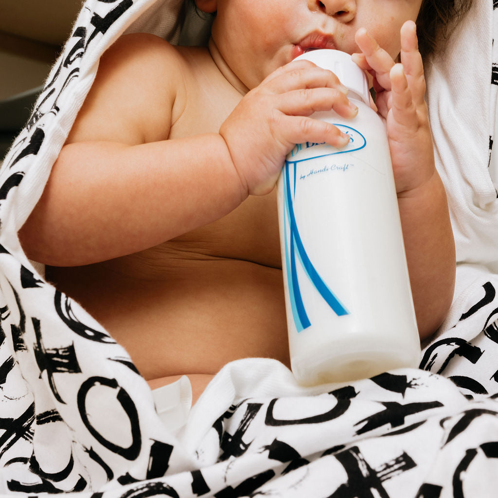 Baby drinking from a bottle wrapped in a patterned blanket