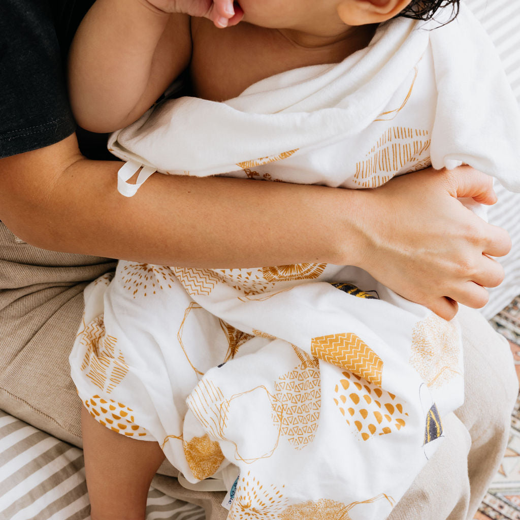 Child wrapped in a patterned blanket being held by an adult on a rug.