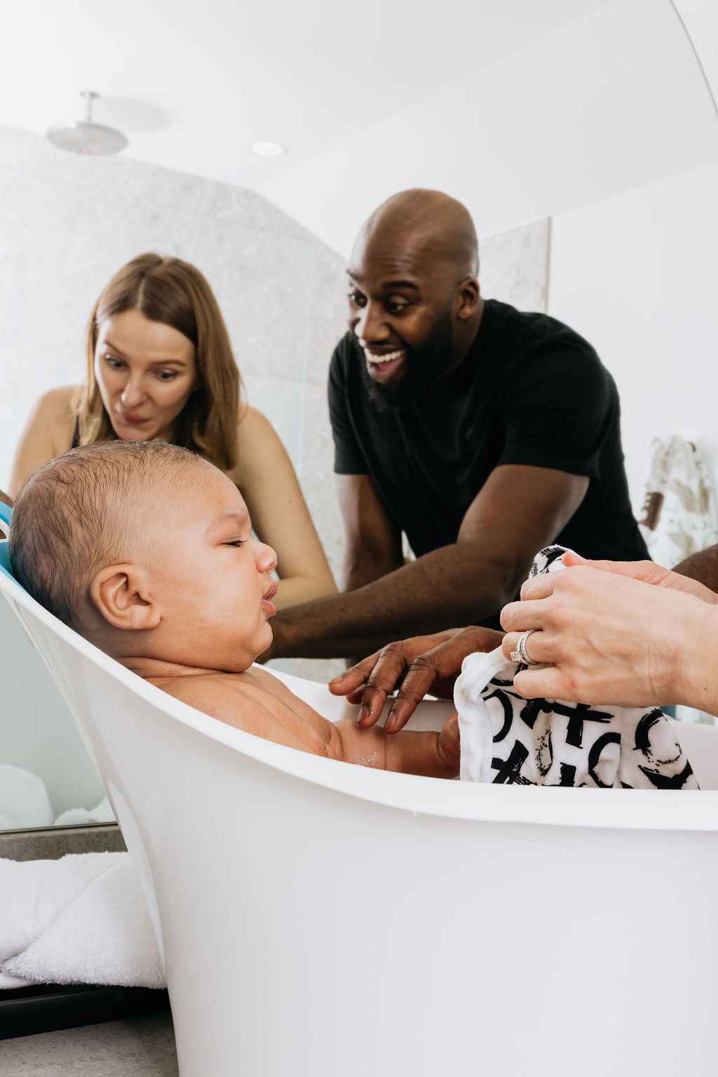 Parents bathing their baby together in a small tub