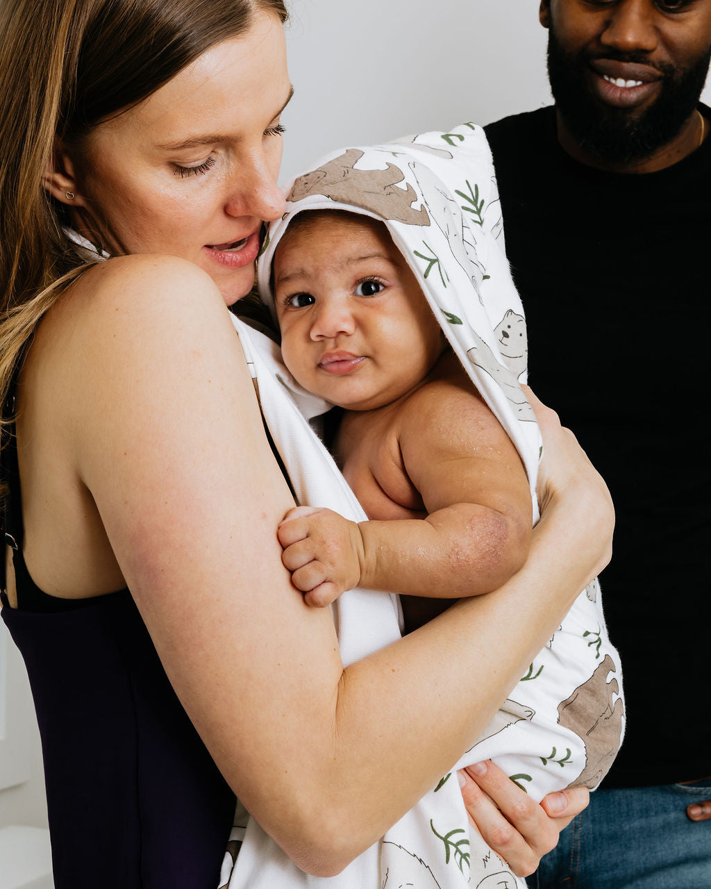 Mom holding her baby in a hooded Oneberrie towel, dad beside them