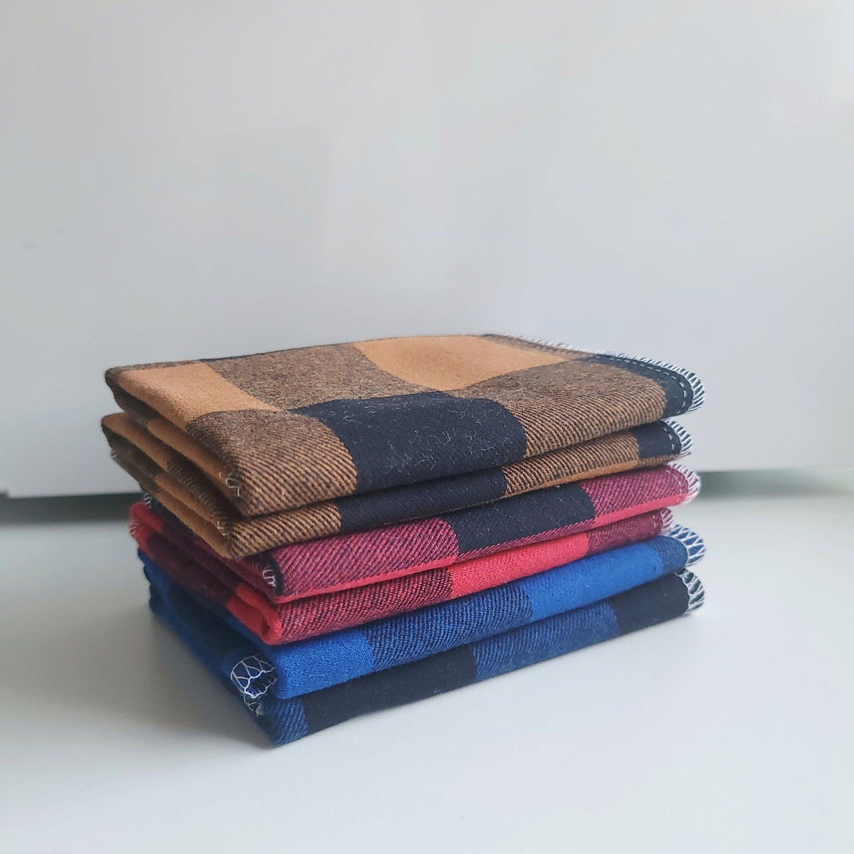 A set of cloth wipes with three plaid patterns, brown, red and blue black, displayed both folded and unfolded.