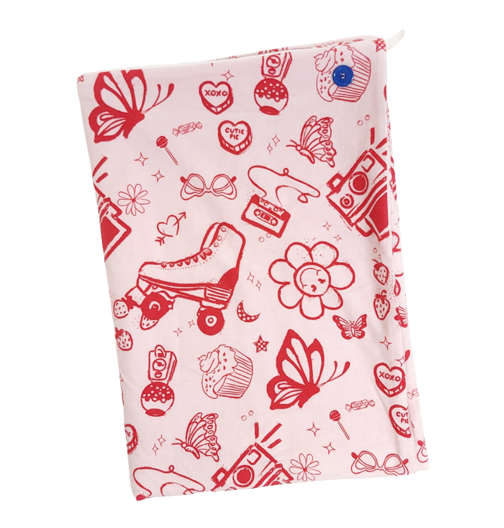 A soft baby towel with a red retro print of hearts, butterflies, rollerskates, flowers and a cassette tape on a pink background 