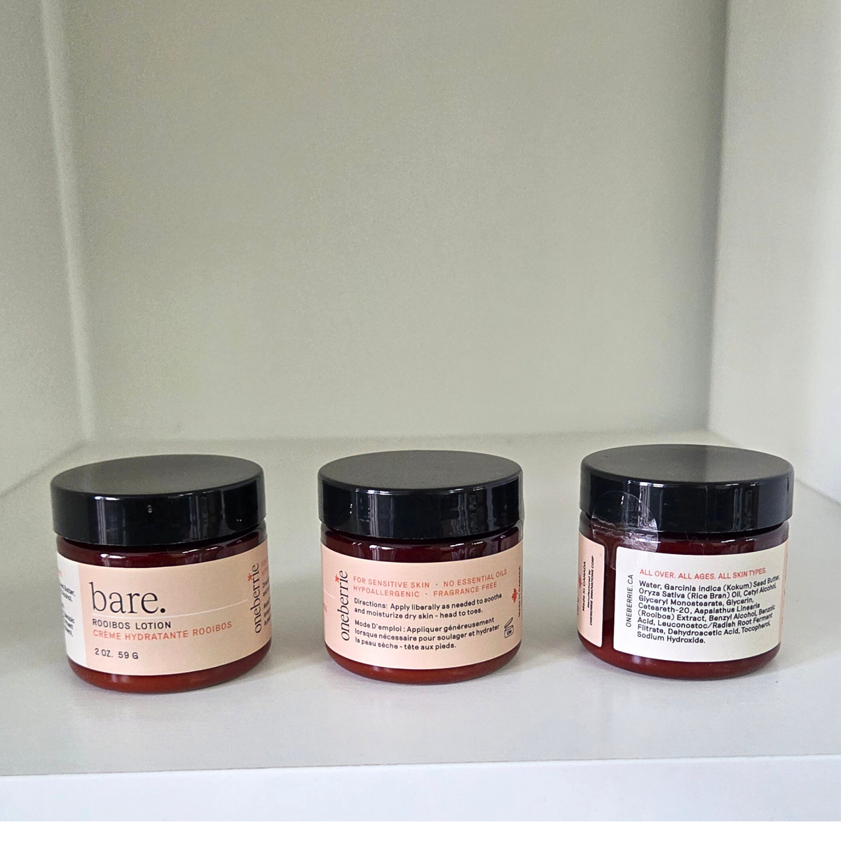 Three jars of 2oz Bare. Lotions, on a white shelf with a neutral background
