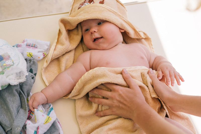 Baby in a regular hooded bath towel after the bath, with arms, chest and legs left uncovered