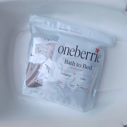 A sealed white pouch of Oneberrie Bath to Bed bedding sits inside a white plastic container. The front label shows the Oneberrie brand name, a small illustrated figure, and product text including 'Bath to Bed' and 'for bath & bed.