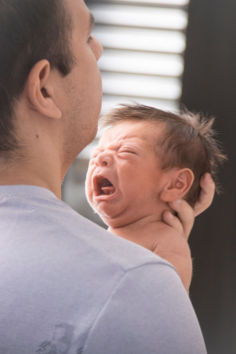 Wet newborn crying over a parent’s shoulder right after the bath